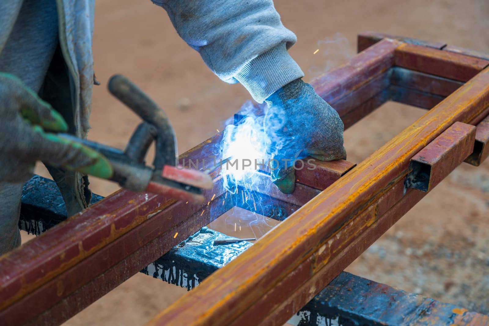 Welder welding two iron profiles at the construction site on a sunny day