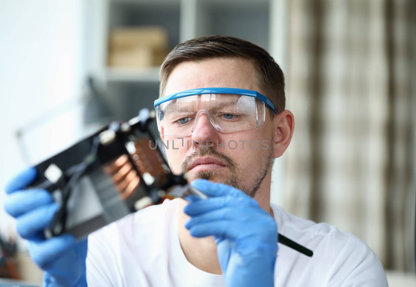 Close-up view of concentrated male in protective eyewear and gloves using forceps for tiny details. Hobby for middle-aged man. Diy and repairman concept