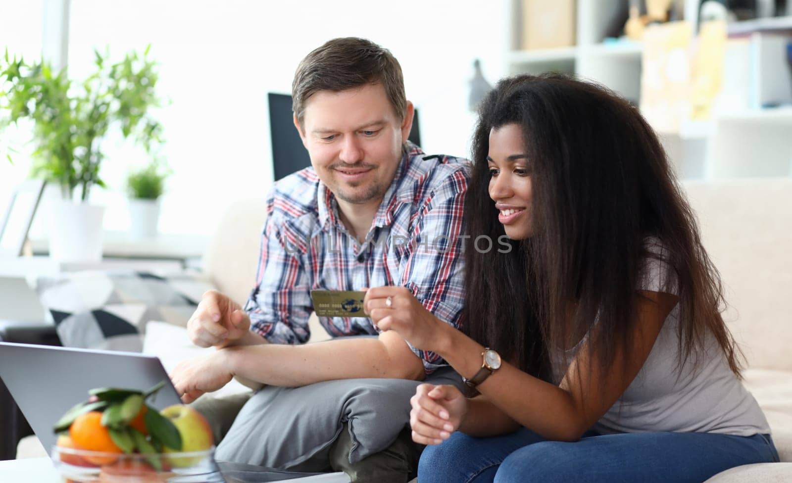 Portrait of beautiful afro-american woman smiling and holding credit card. Middle-aged man using laptop. Couple going to pay via internet. Online shopping concept