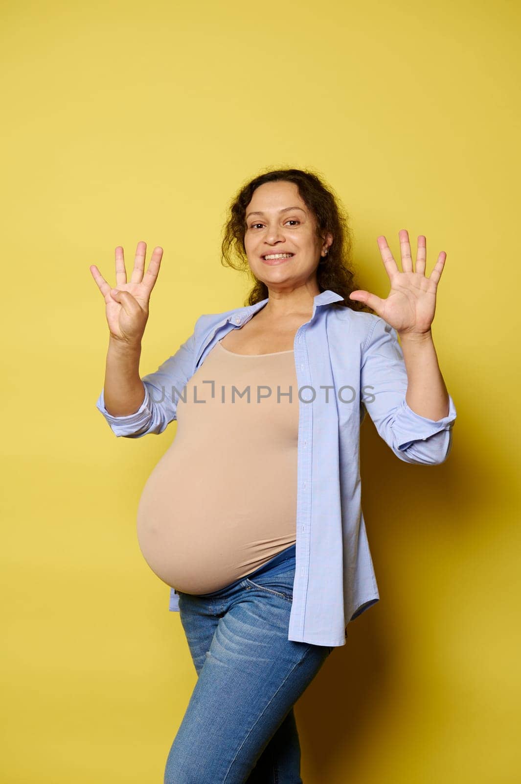 Smiling pregnant woman expecting a baby, showing nine fingers at camera. She's in last trimester of her happy pregnancy. by artgf