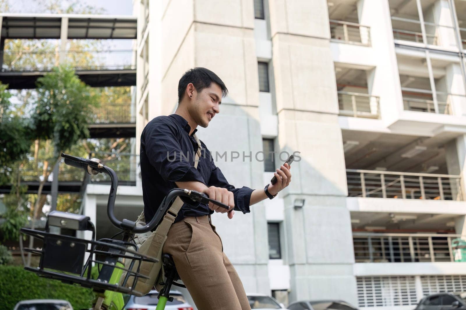 A young Asian businessman rides a bicycle to work. Standing outside the office talking on the phone and talking about business. Concept of reducing energy and reducing air pollution. by wichayada