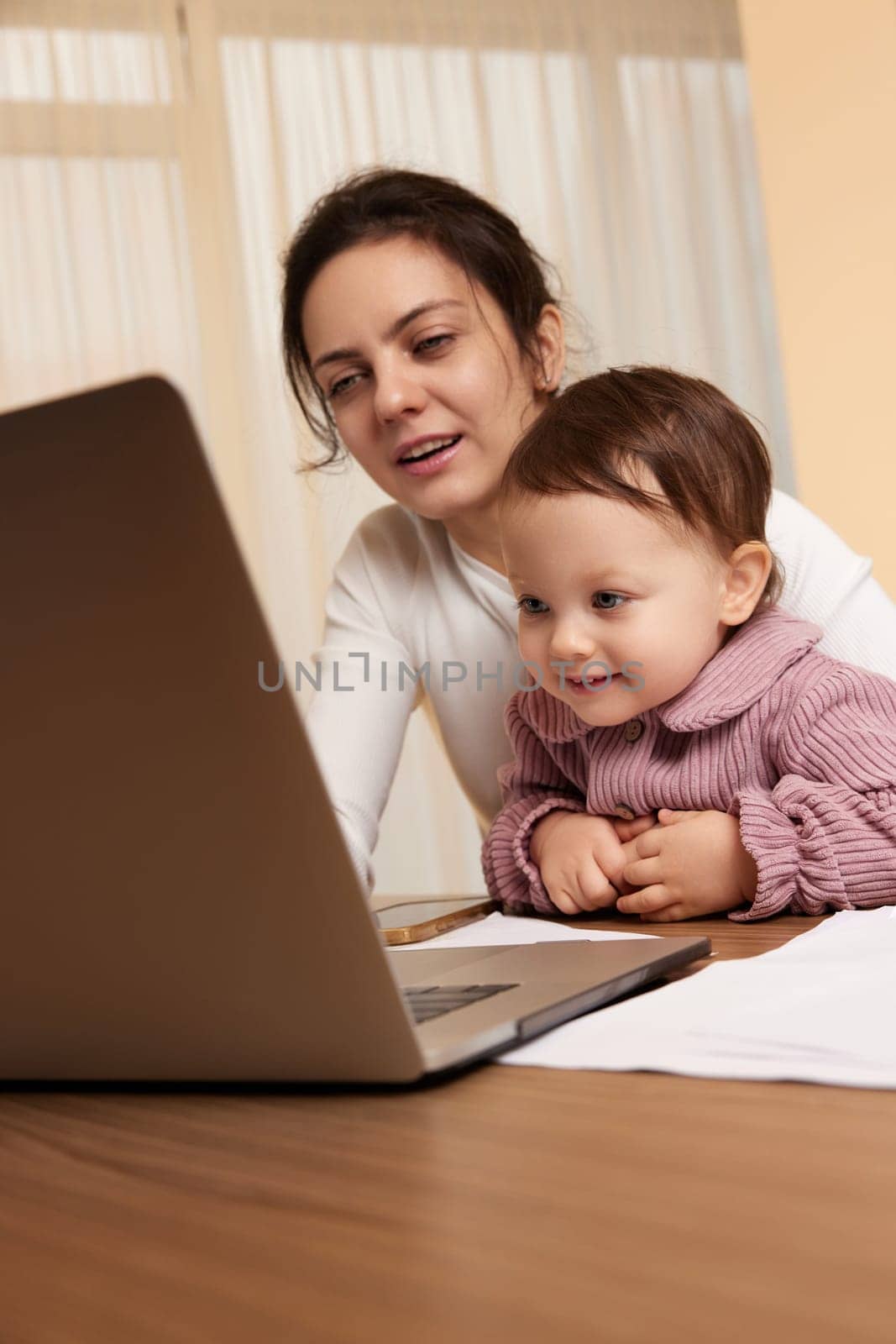 Cheerful pretty businesswoman working at the computer with her little child girl at home