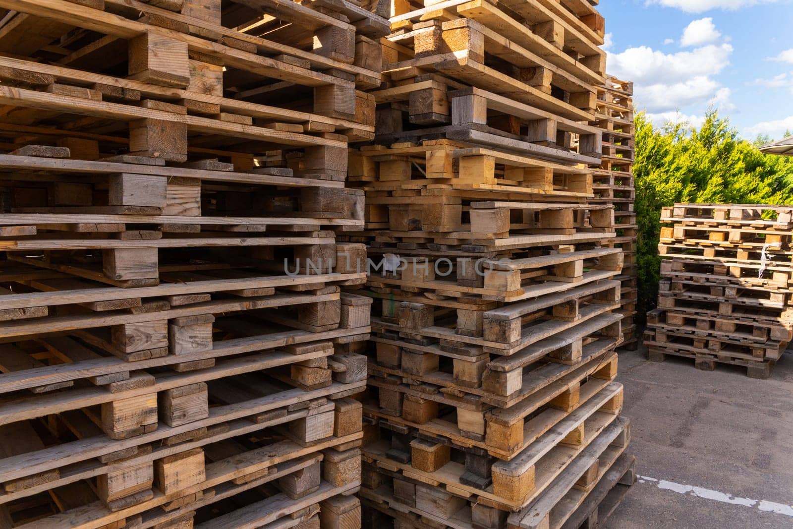 Piles of stacked natural wooden shipping pallets. Outside a big stack with big stack of wooden pallets.