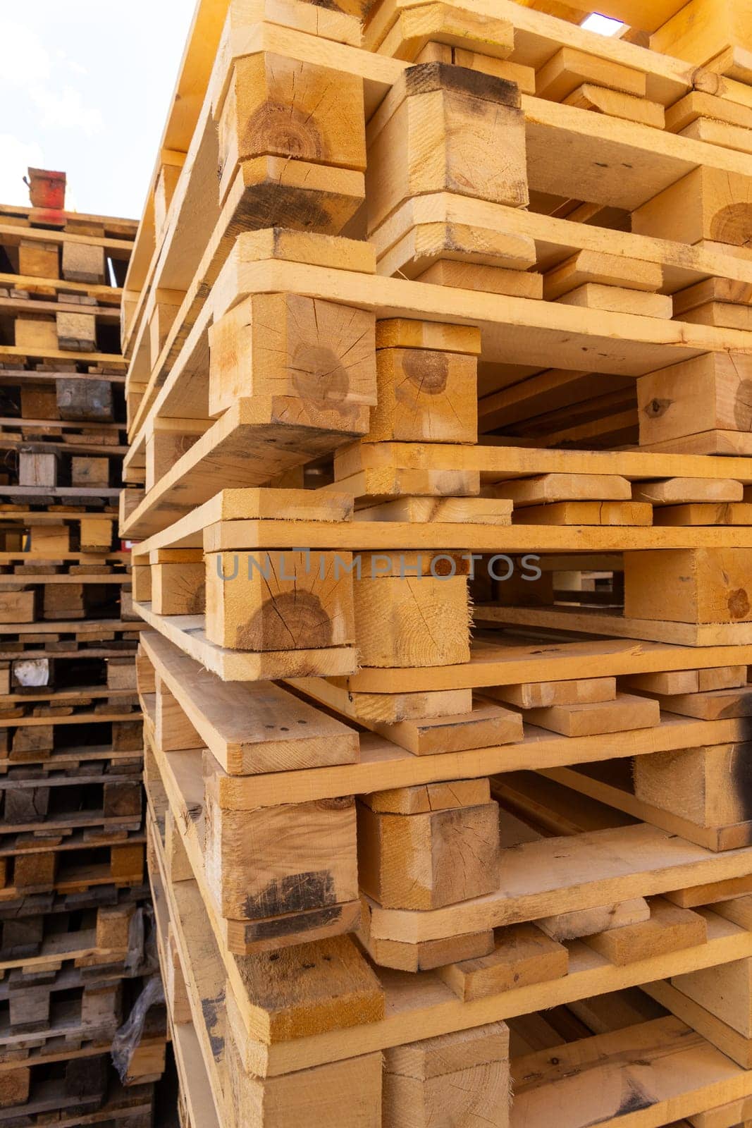 Piles of stacked natural wooden shipping pallets. Outside a big stack with big stack of wooden pallets.