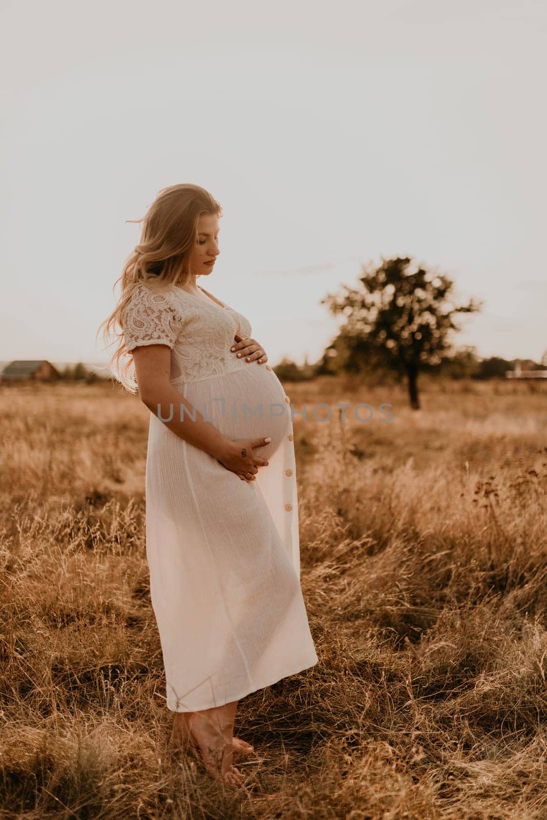 Caucasian pregnant young blonde woman in cotton white linen dress stand walking in meadow by AndriiDrachuk