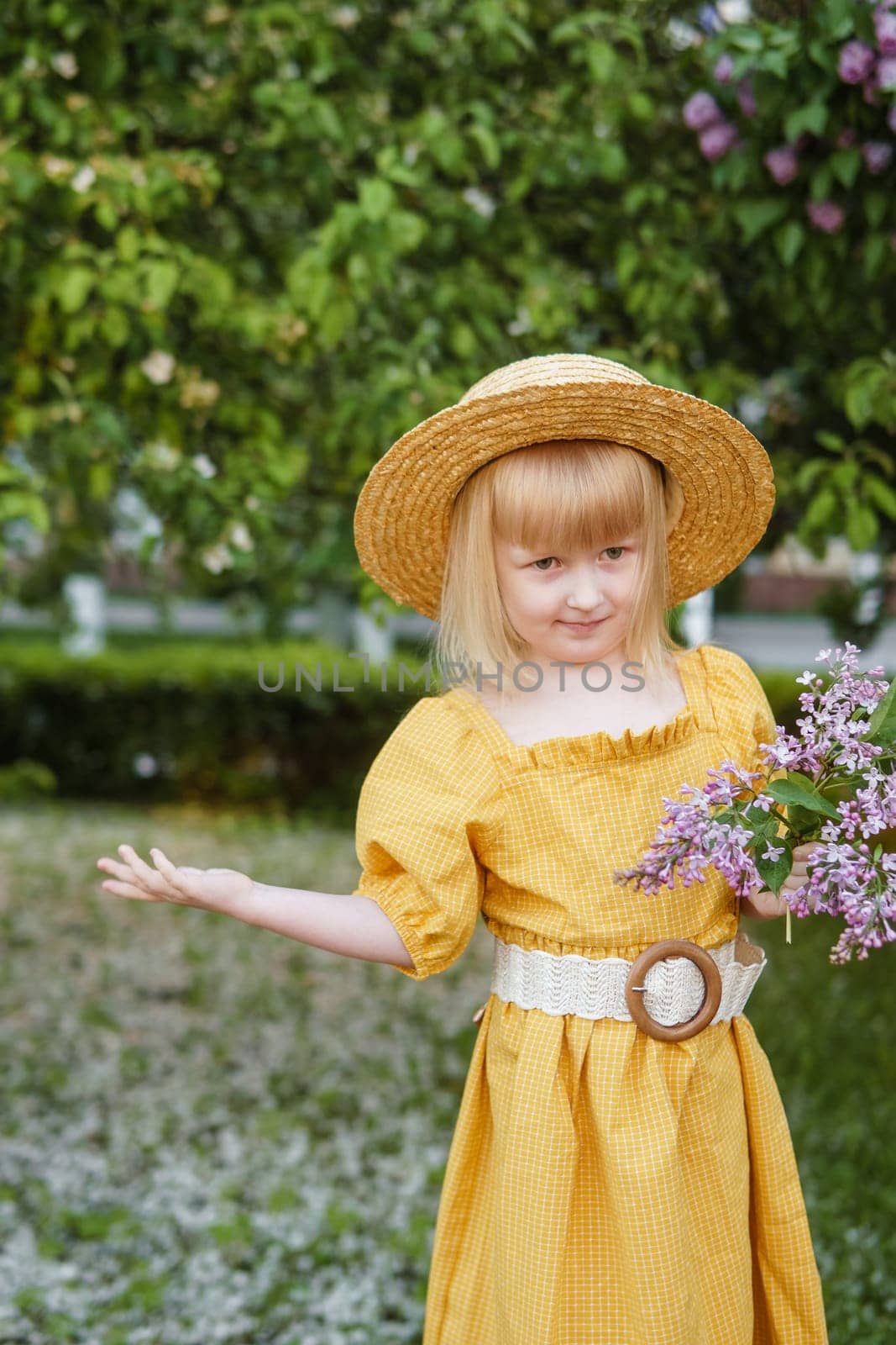 A little girl in a yellow dress and straw hat wearing a bouquet of lilacs. A walk in a spring park, blossoming lilacs. by Annu1tochka
