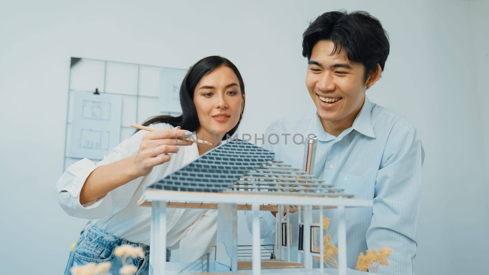 Professional young beautiful architect engineer using ruler and pencil measuring model roof length at modern office with blueprint hanged behind. Creative design and teamwork concept. Immaculate.