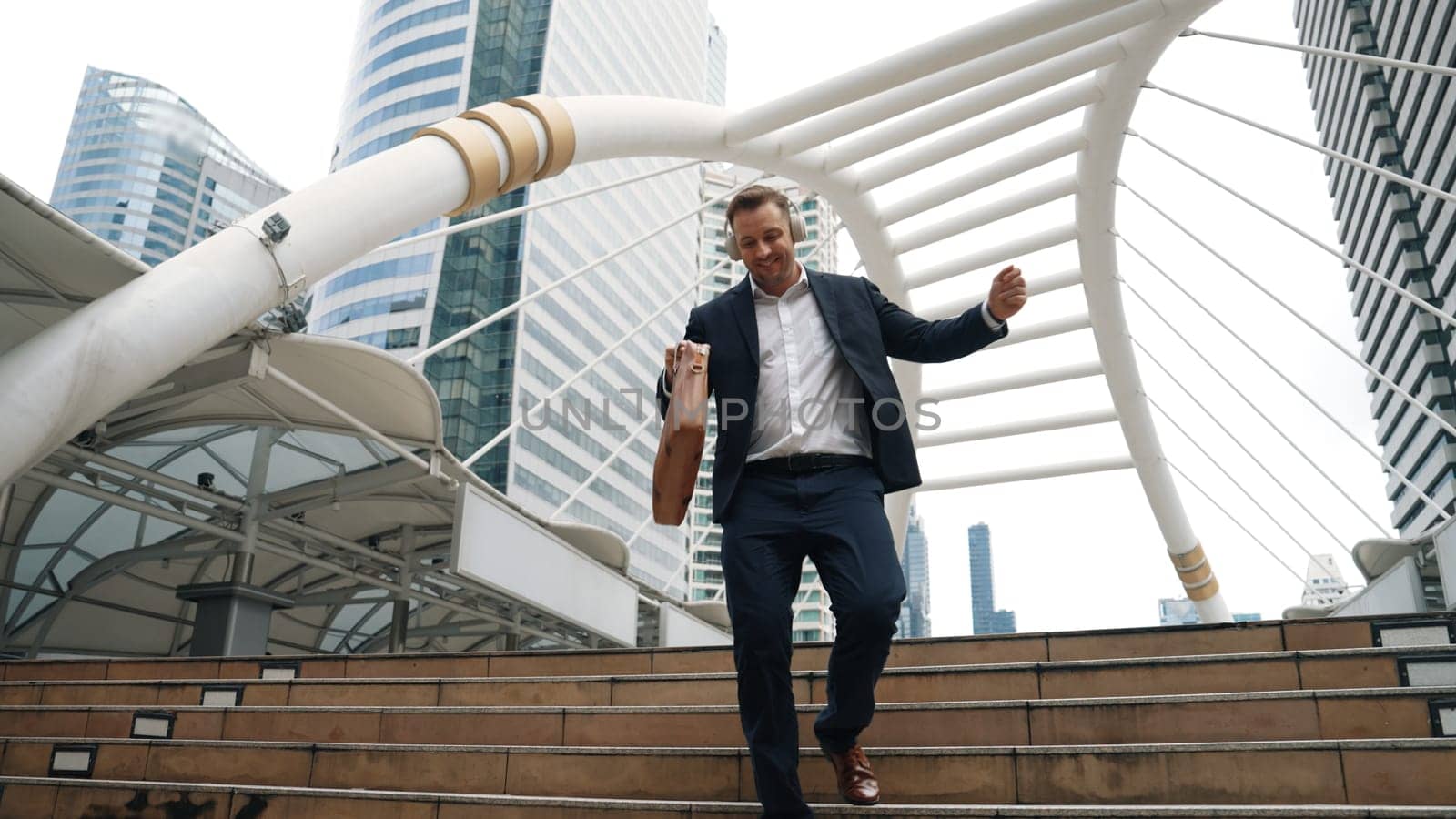 Happy businessman walking down stair and moving to music from headphone. Urbane. by biancoblue