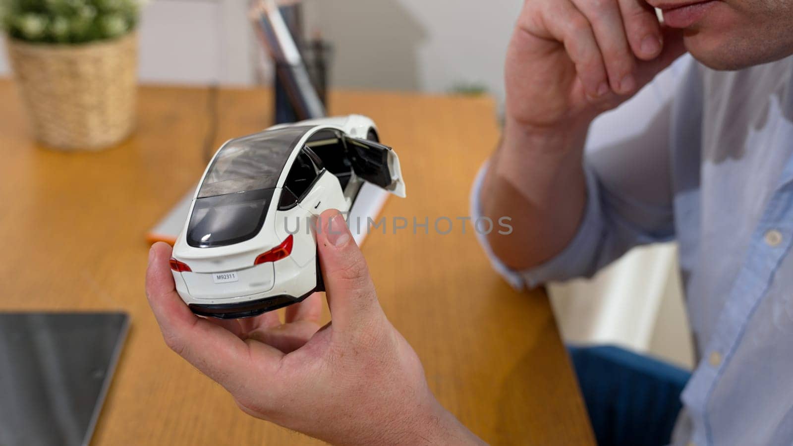 Car design engineer analyze car model prototype for automotive business company at home office. Vehicle designer holding scale car, carefully analyzing looking for any flaw or improvement. Synchronos