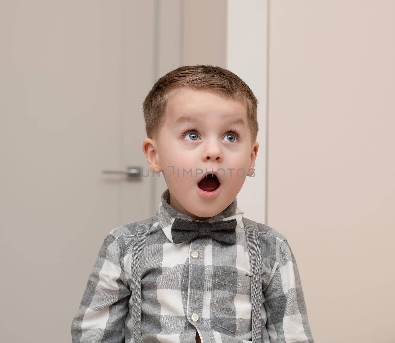 Emotions of surprise and delight on the child s face. A small handsome boy of 4 years old in a shirt with a bow tie shows a grimace with an expression on his face. Close-up. by ketlit