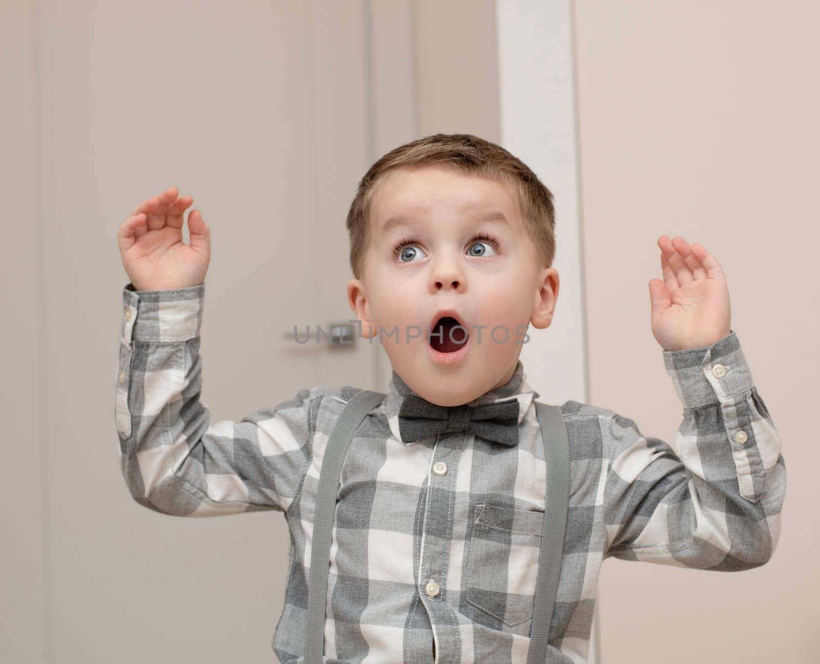 Emotions of surprise and delight on the child s face. A small handsome boy of 4 years old in a shirt with a bow tie shows a grimace with an expression on his face. Close-up. by ketlit