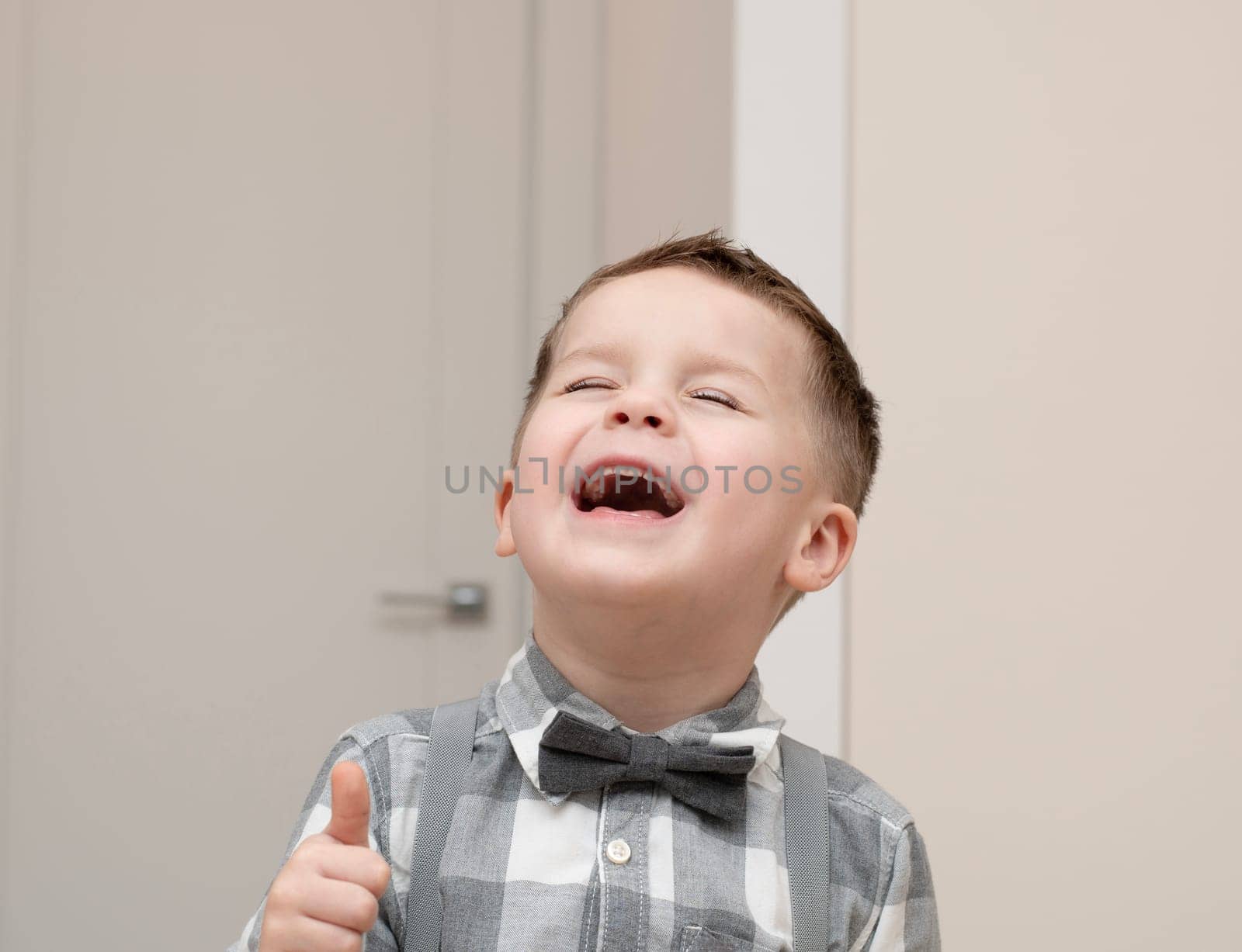 Emotions of happiness, fun, joy and delight on the child s face. A small handsome boy of 4 years old in a shirt with a bow tie shows a mime with a facial expression. Close-up. portrait