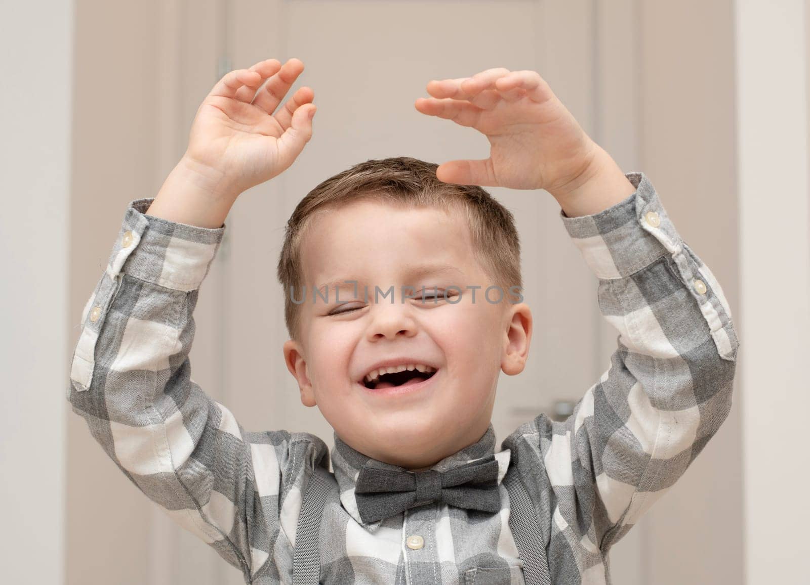 Emotions of happiness, fun, joy and delight on the child s face. A small handsome boy of 4 years old in a shirt with a bow tie shows a mime with a facial expression. by ketlit