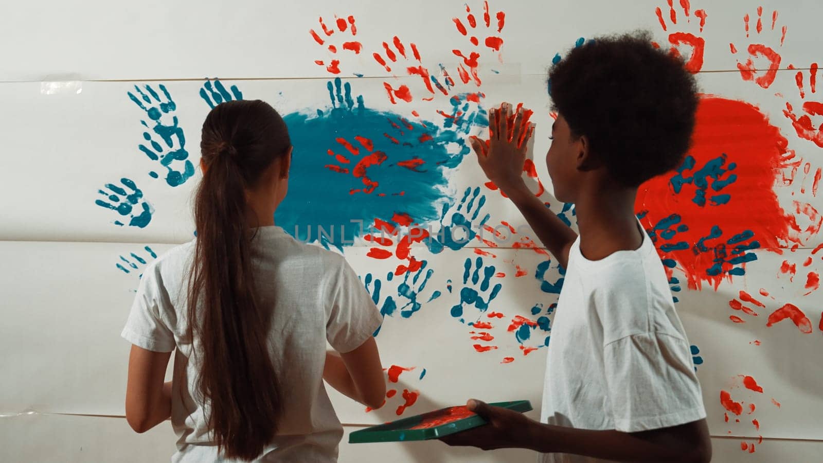 Highschool girl and african boy paint the wall with their hand. Edification. by biancoblue