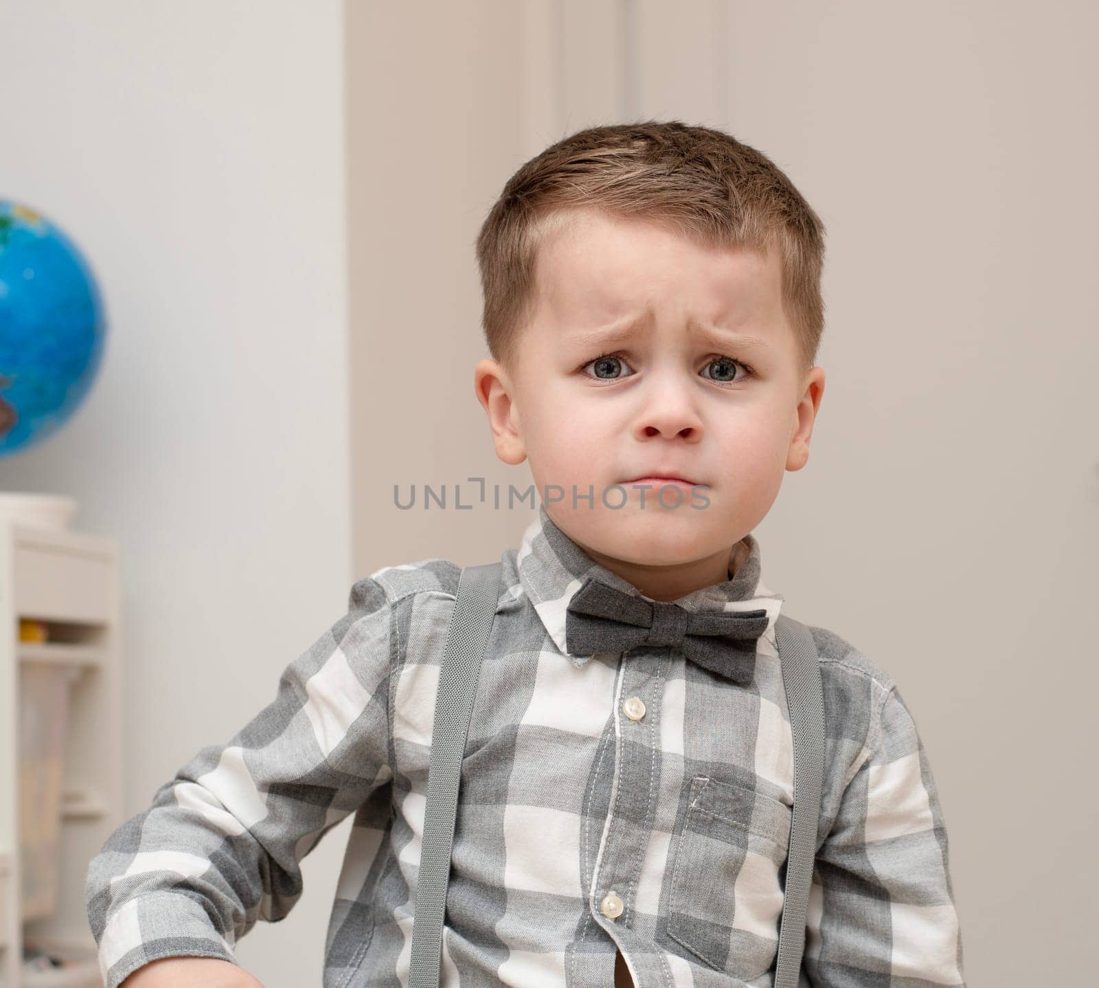 Emotions of sadness, resentment, sadness on the child s face. A small handsome boy of 4 years old in a shirt with a bow tie shows facial expressions. by ketlit
