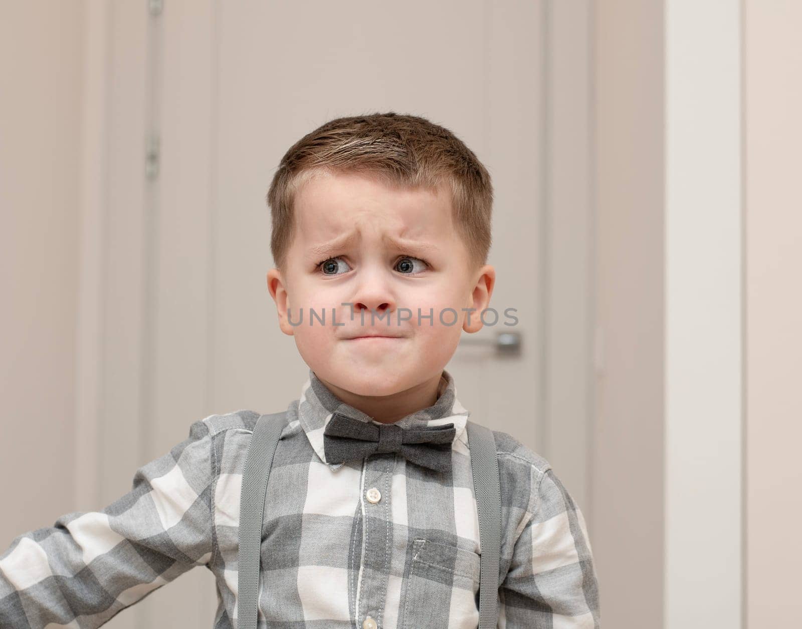 Emotions of sadness, resentment, sadness on the child s face. A small handsome boy of 4 years old in a shirt with a bow tie shows facial expressions. by ketlit