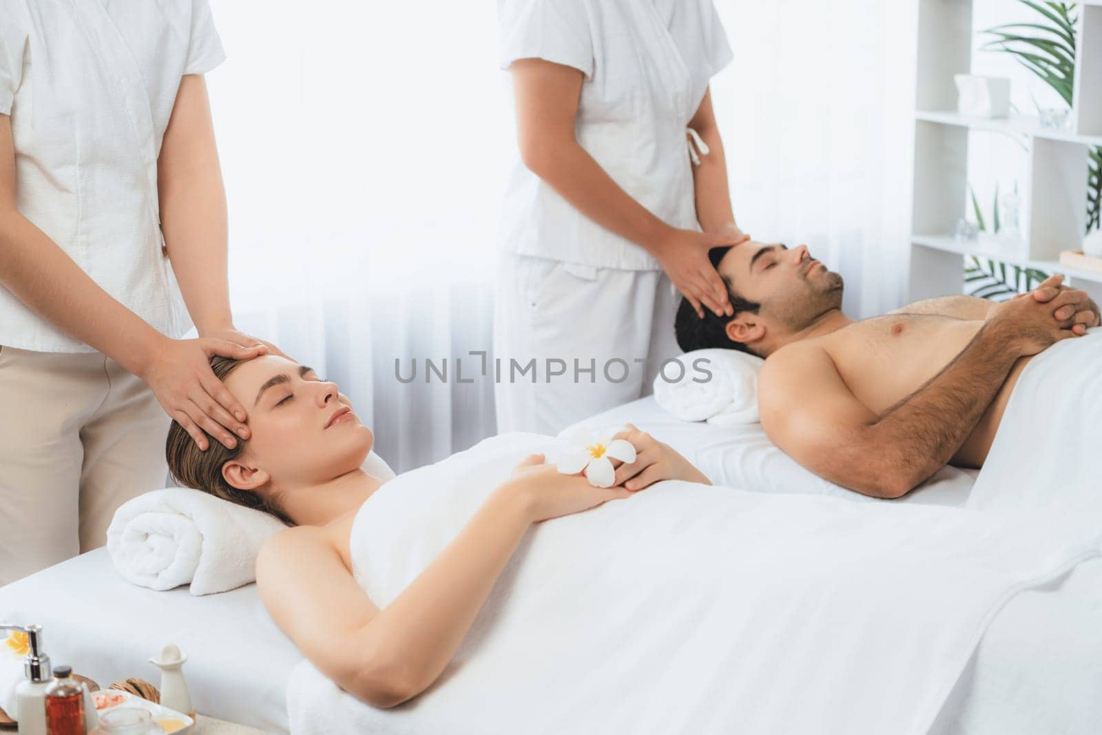 Caucasian couple enjoying relaxing anti-stress head massage and pampering facial beauty skin recreation leisure in dayspa modern light ambient at luxury resort or hotel spa salon. Quiescent