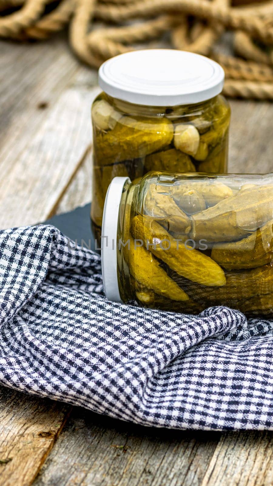 Glass jars with pickled red bell peppers and pickled cucumbers (pickles) isolated. Jars with variety of pickled vegetables. Preserved food concept in a rustic composition. by vladispas