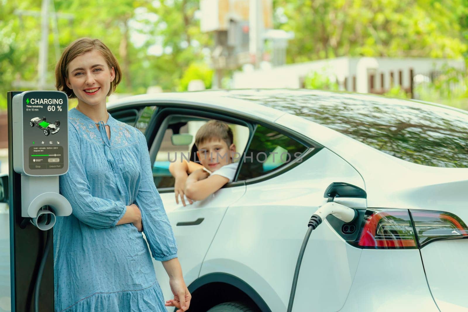 Environmental awareness family with eco-friendly electric car recharging battery from home EV charging station with little boy inside the car. Rechargeable and EV car technology. Perpetual