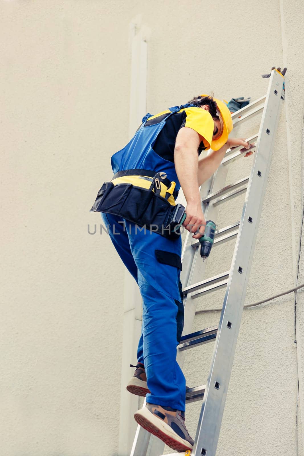 Serviceman holds drill climbing ladder by DCStudio
