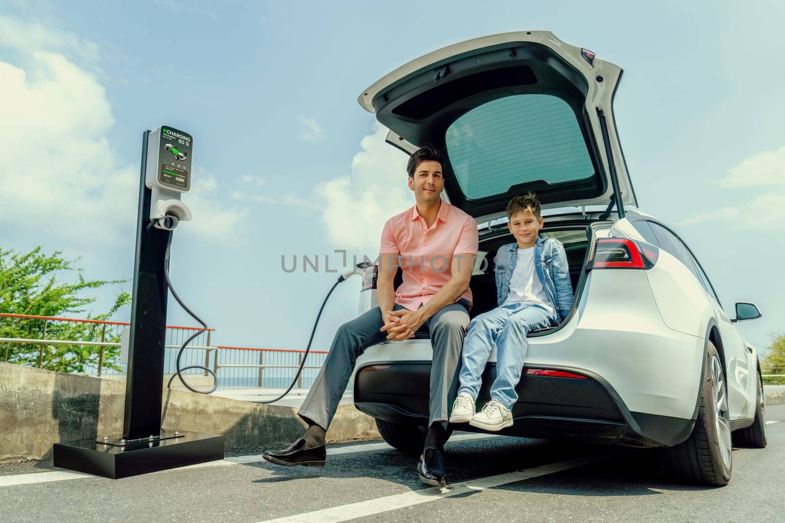 Family road trip vacation traveling by the sea with electric car, father and son recharge EV car with green and clean energy. Natural travel and eco-friendly car for sustainable environment. Perpetual