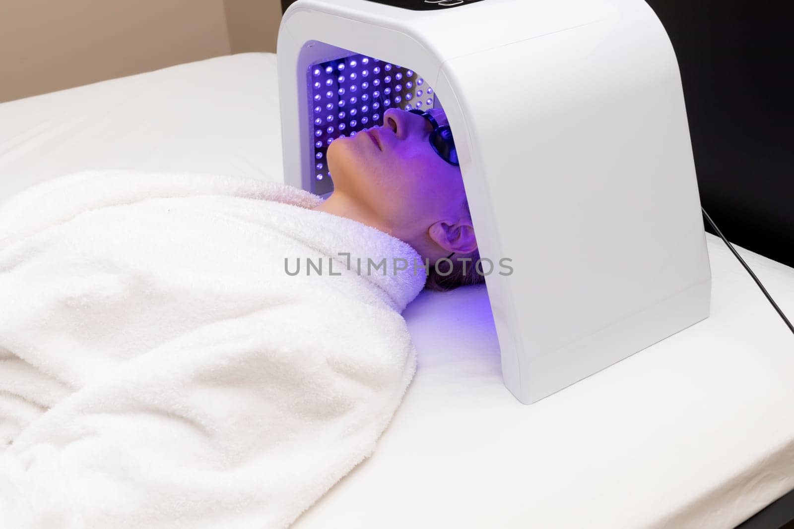 Home Skin Care Procedure. Cosmetic Led Light Face Mask. Woman In Her 30s Lying Under Facial Regenerative Treatment Mask On Bed In Bedroom. Acne, Spot Cure. Beauty Photon Therapy. Horizontal Plane by netatsi