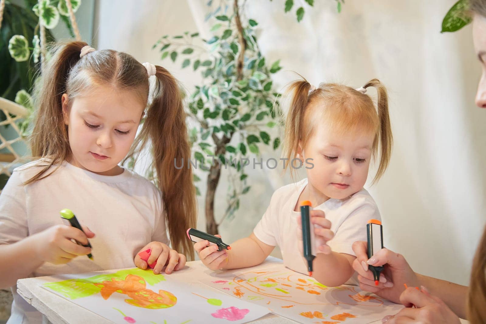 Cute little sisters are painting on table. Preschooler, 4 and 8 years child in living room. Small girl kids doing homework. Home schooling concept by keleny