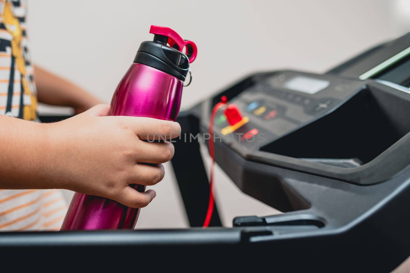 Young girl running on the treadmill with a sports water bottle in hand by Sonat