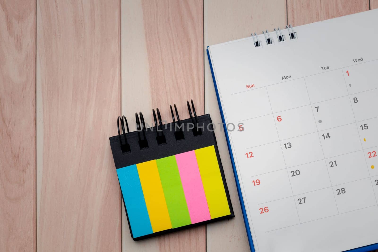 Top view of desk calendar and index sticky note on wooden table background with copy space. by iamnoonmai