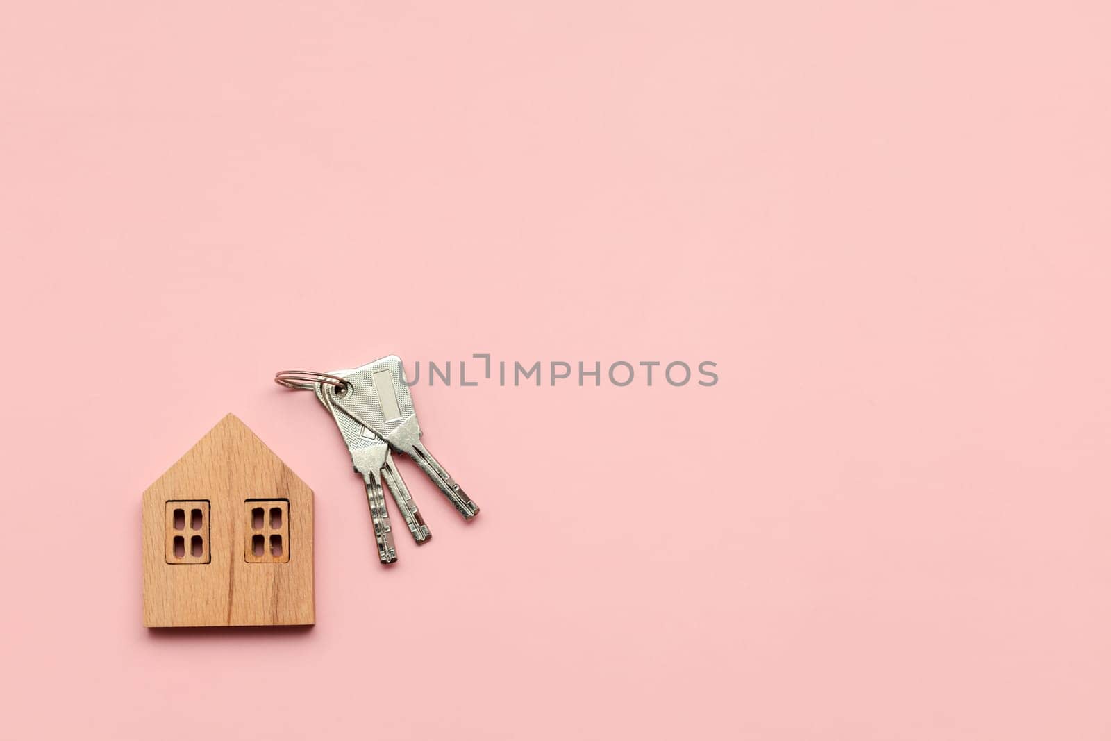 Wooden house model with keys on pink background. Mortgage concept. by iamnoonmai