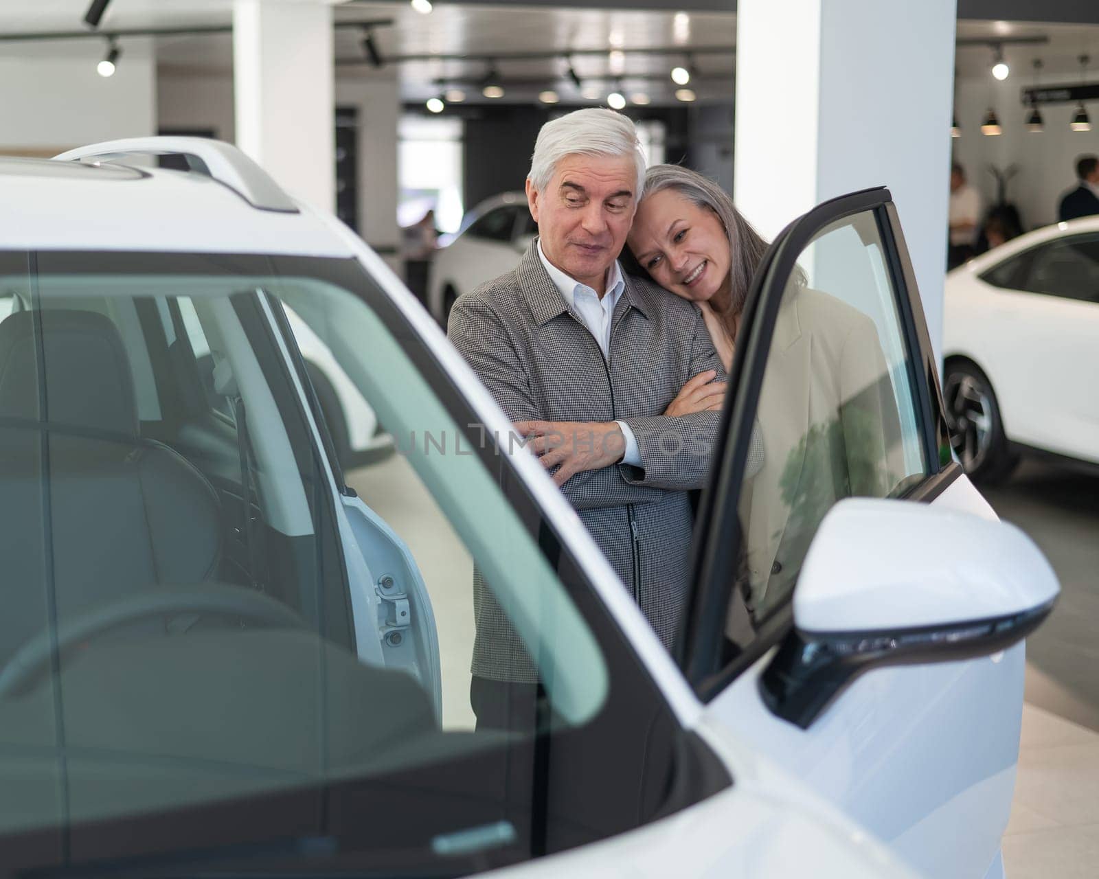 An elderly Caucasian couple chooses a new car at a car dealership. by mrwed54