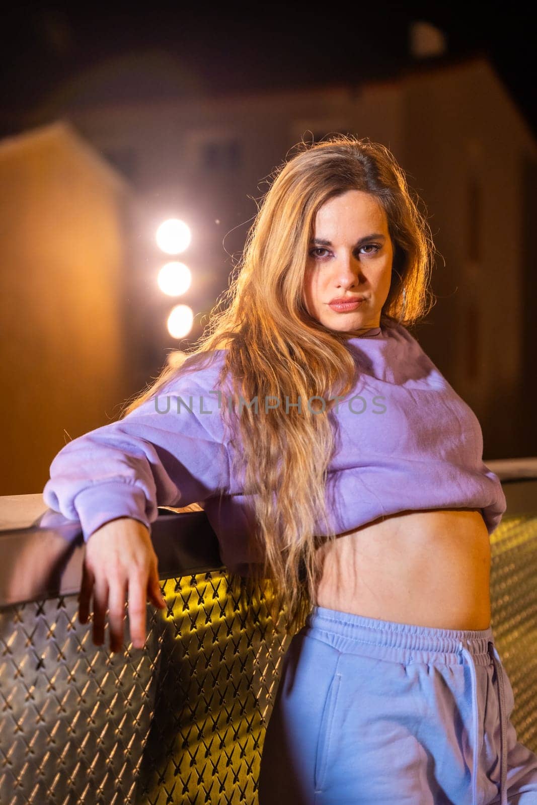 Vertical portrait of a blonde female rude trap dancer posing in the street at night