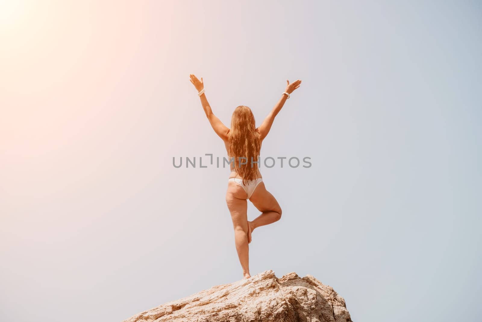 Woman sea yoga. Back view of free calm bliss satisfied woman with long hair standing on top rock with yoga position against of sky by the sea. Healthy lifestyle outdoors in nature, fitness concept. by panophotograph