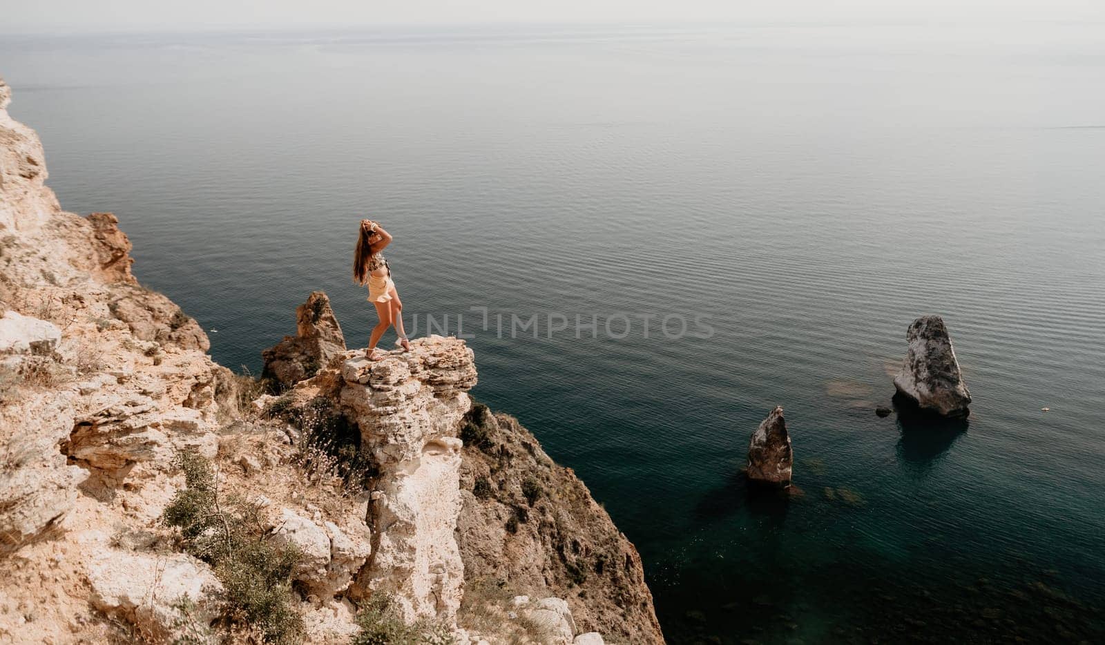 Woman travel sea. Happy tourist taking picture outdoors for memories. Woman traveler looks at the edge of the cliff on the sea bay of mountains, sharing travel adventure journey.