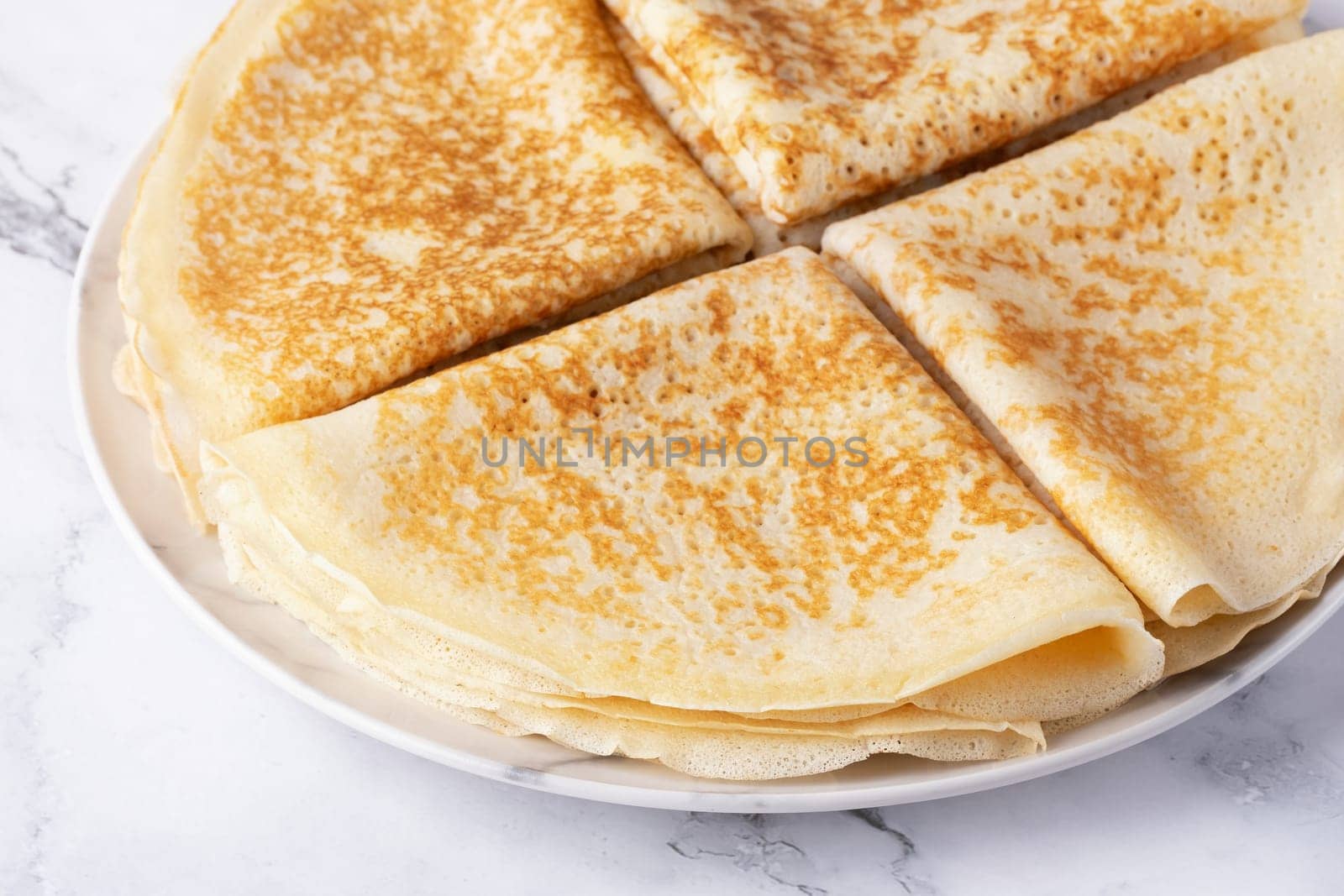 A stack of thin pancakes on a light marble table.