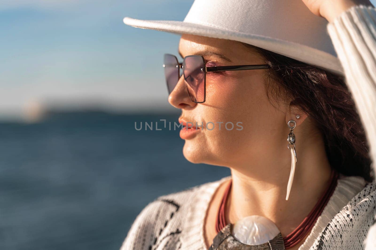 Portrait of a curly haired woman in a white hat and glasses on the background of the sea
