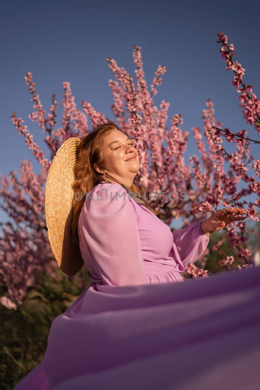 Woman blooming peach orchard. Against the backdrop of a picturesque peach orchard, a woman in a long pink dress and hat enjoys a peaceful walk in the park, surrounded by the beauty of nature. by Matiunina