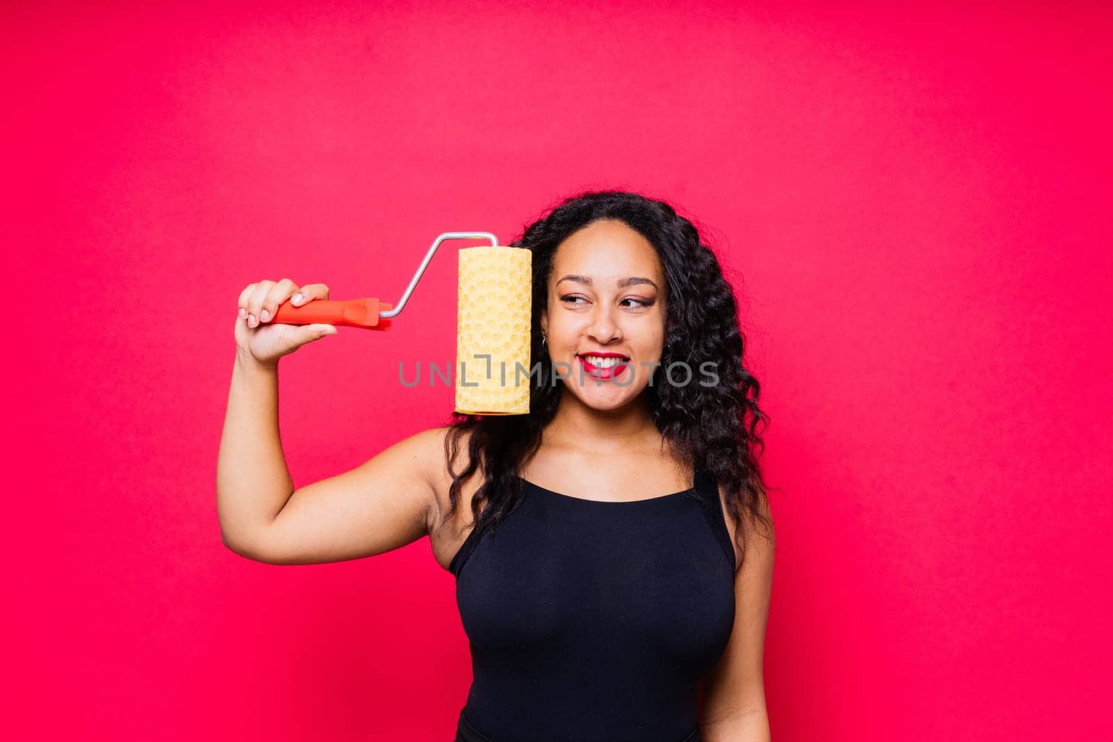 Happy young African woman with paintroller, toothy smile during home renovation by Zelenin