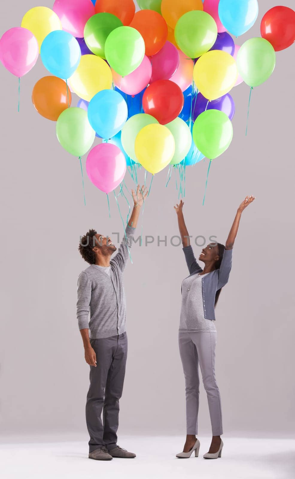 Happy couple, party and celebration with balloons for event, birthday or romance on a gray studio background. Excited man and woman with colorful blowups of helium for date, giveaway or anniversary by YuriArcurs