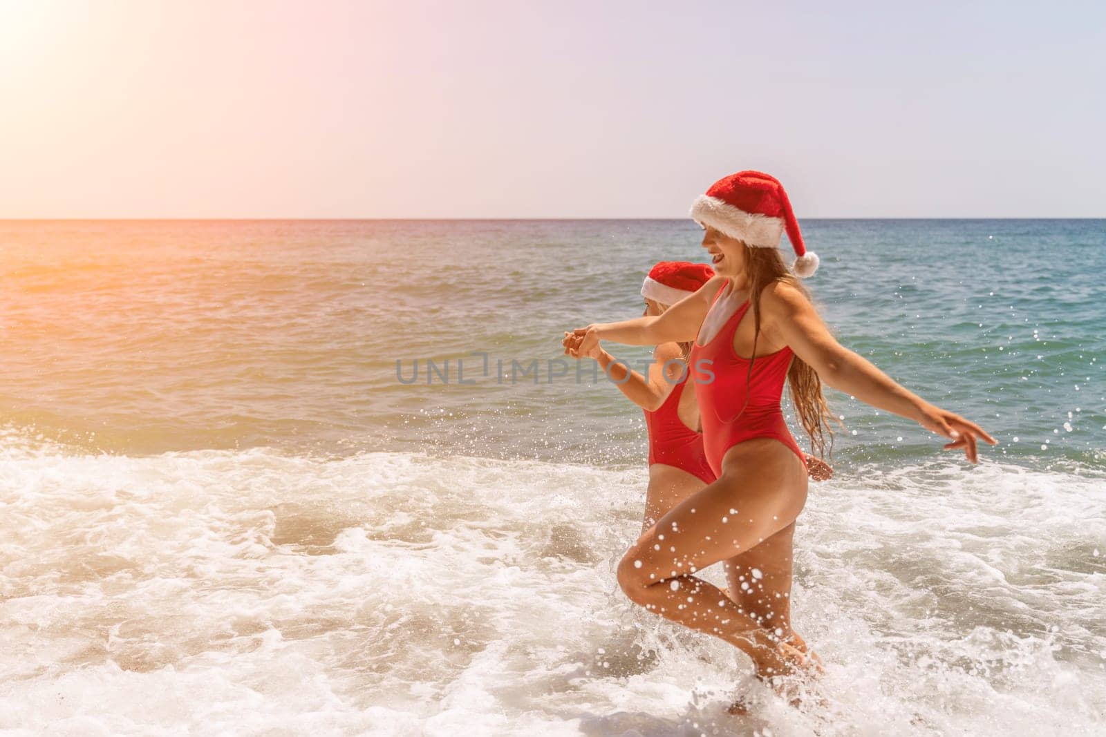 Women in Santa Claus hats run into the sea dressed in red swimsuits. Celebrating the New Year in a hot country.