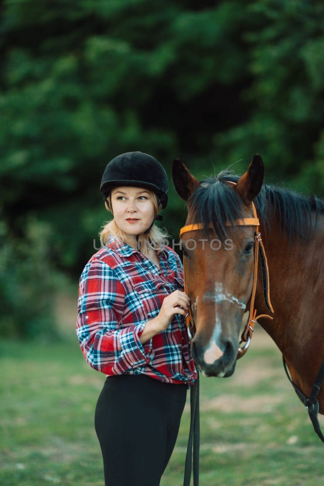 Happy blonde with horse in forest. Woman and a horse walking through the field during the day. Dressed in a plaid shirt and black leggings