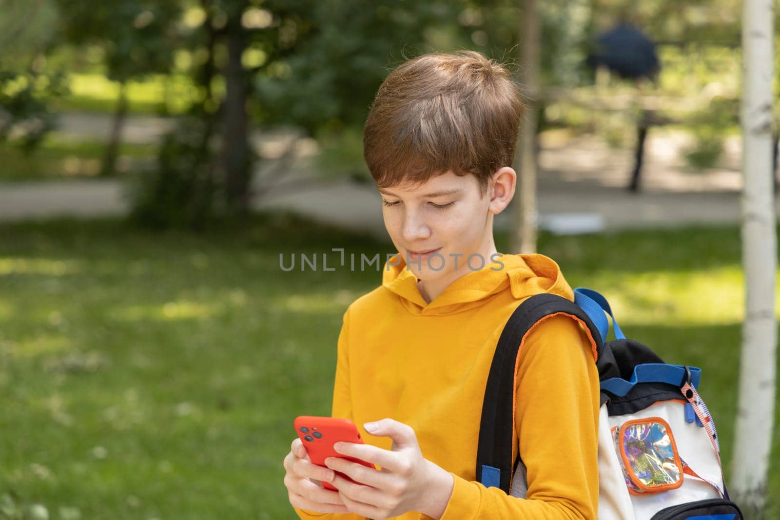 Young boy with dressed yellow hoodie looking at his mobile phone, outdoors spring time. by Ri6ka