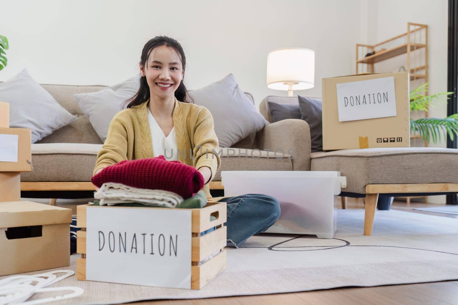 Young Asian women sit in living room sorting clothes for donation in a donation box second hand clothes.