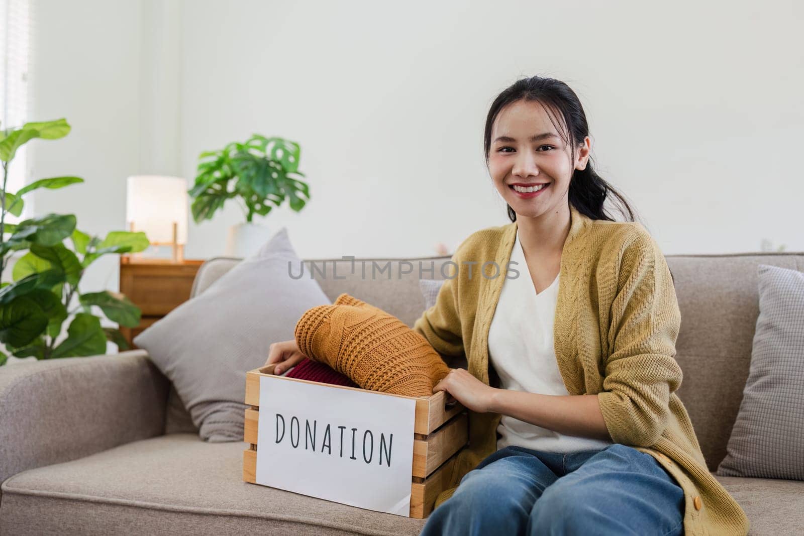 Young Asian women sit in living room sorting clothes for donation in a donation box second hand clothes.