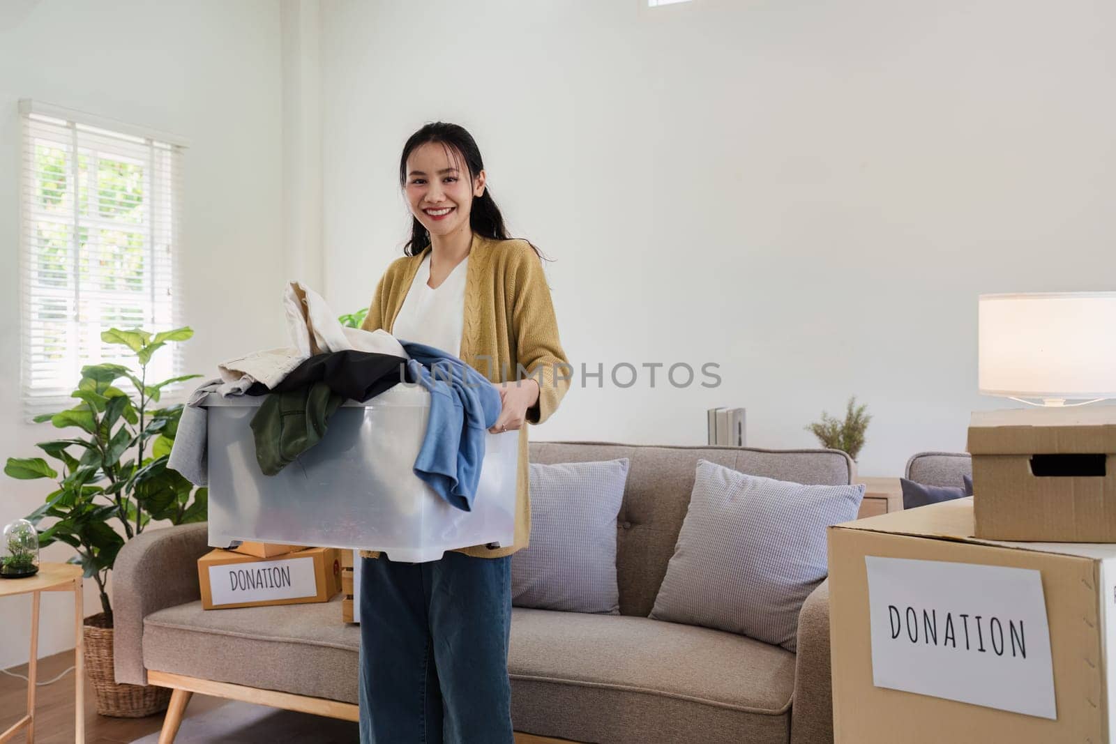 Asian woman holding box full of second hand clothes to donate. Help poor people.