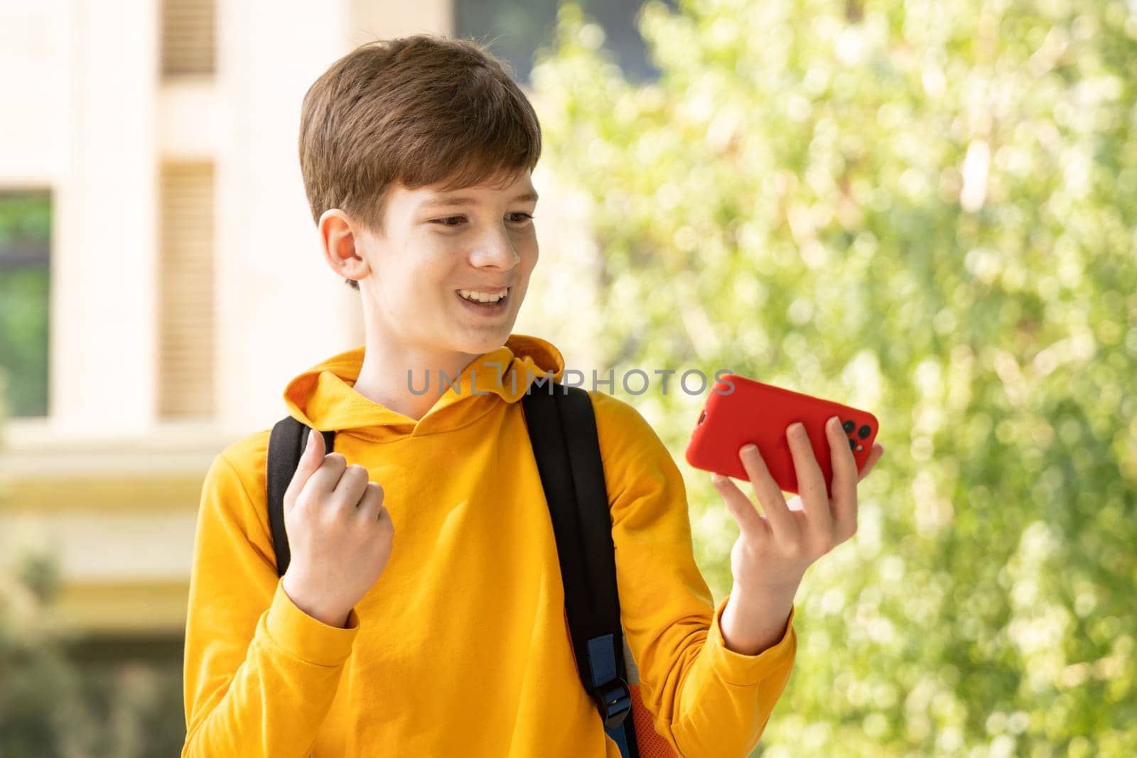 Excited happy teenager boy winner feeling joy smiling and looking at smartphone. Boy using phone, winning lottery game, getting cashback, online gift in app, holding cell phone outdoor