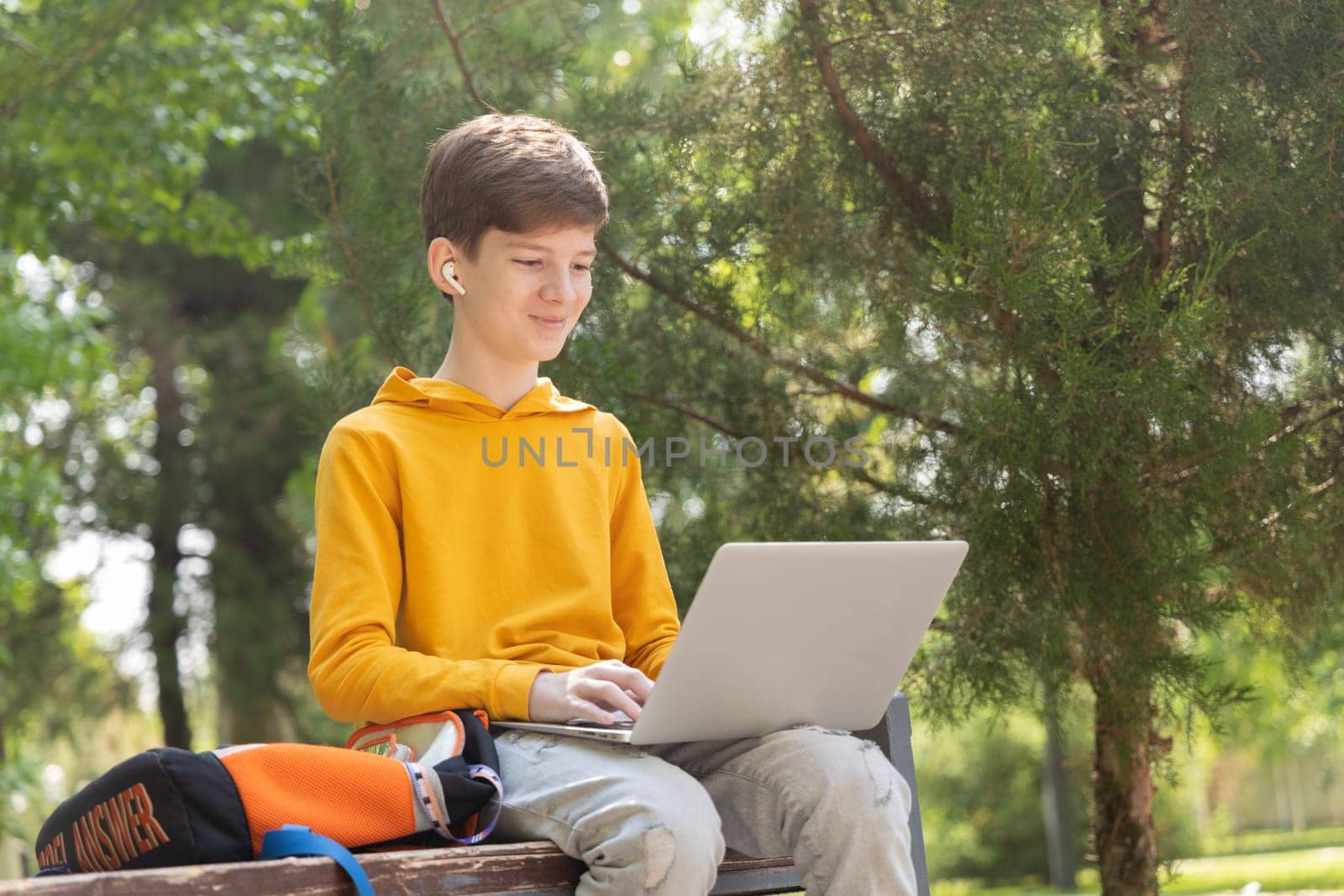 Smiling teenager boy working on laptop. Holding and using a laptop for networking on a sunny spring day, outdoors