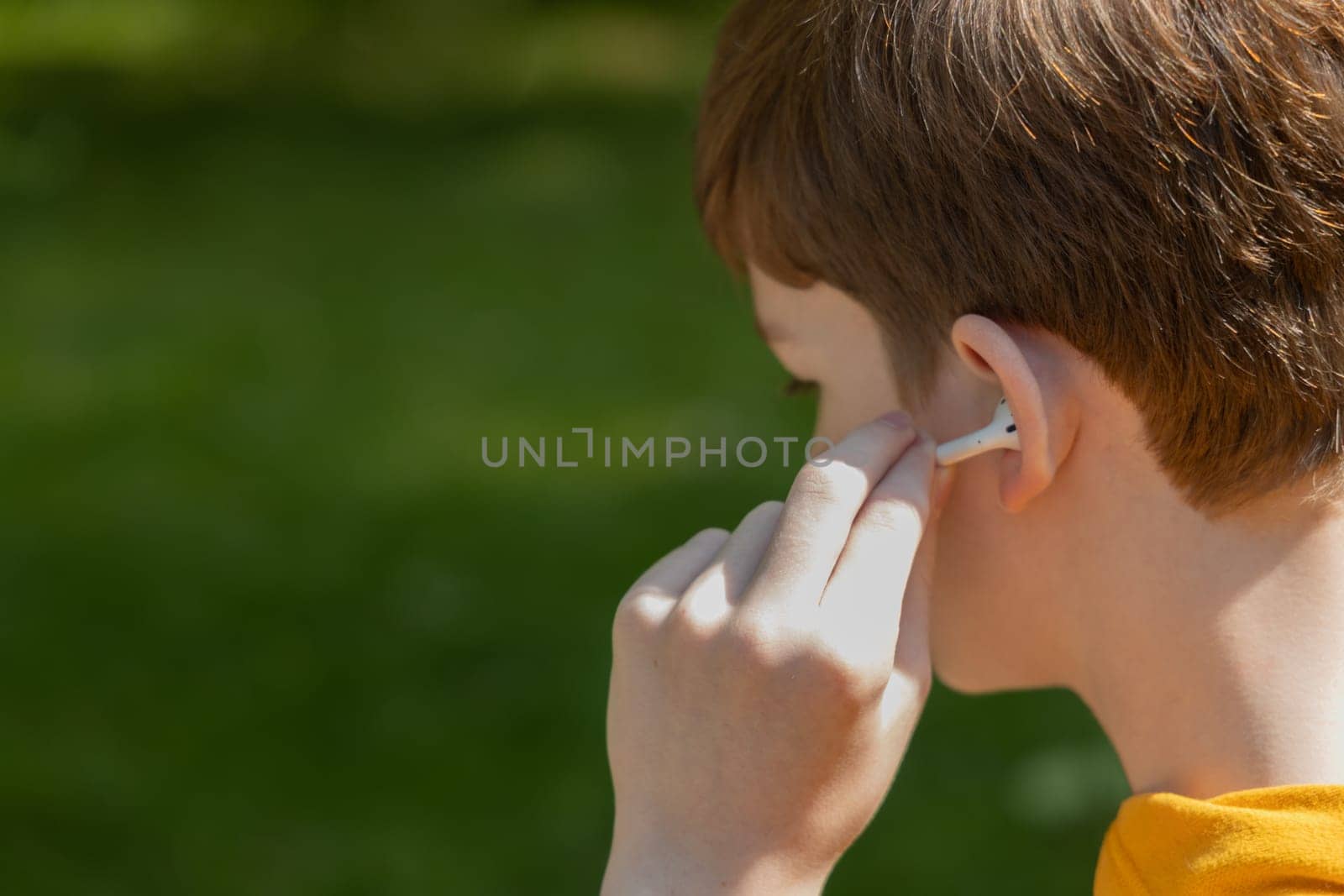 Close up of teenager boy using earbuds outdoor. Lifestyle boy wearing wireless earphones, listening song or audiobook on smartphone, copy space. by Ri6ka