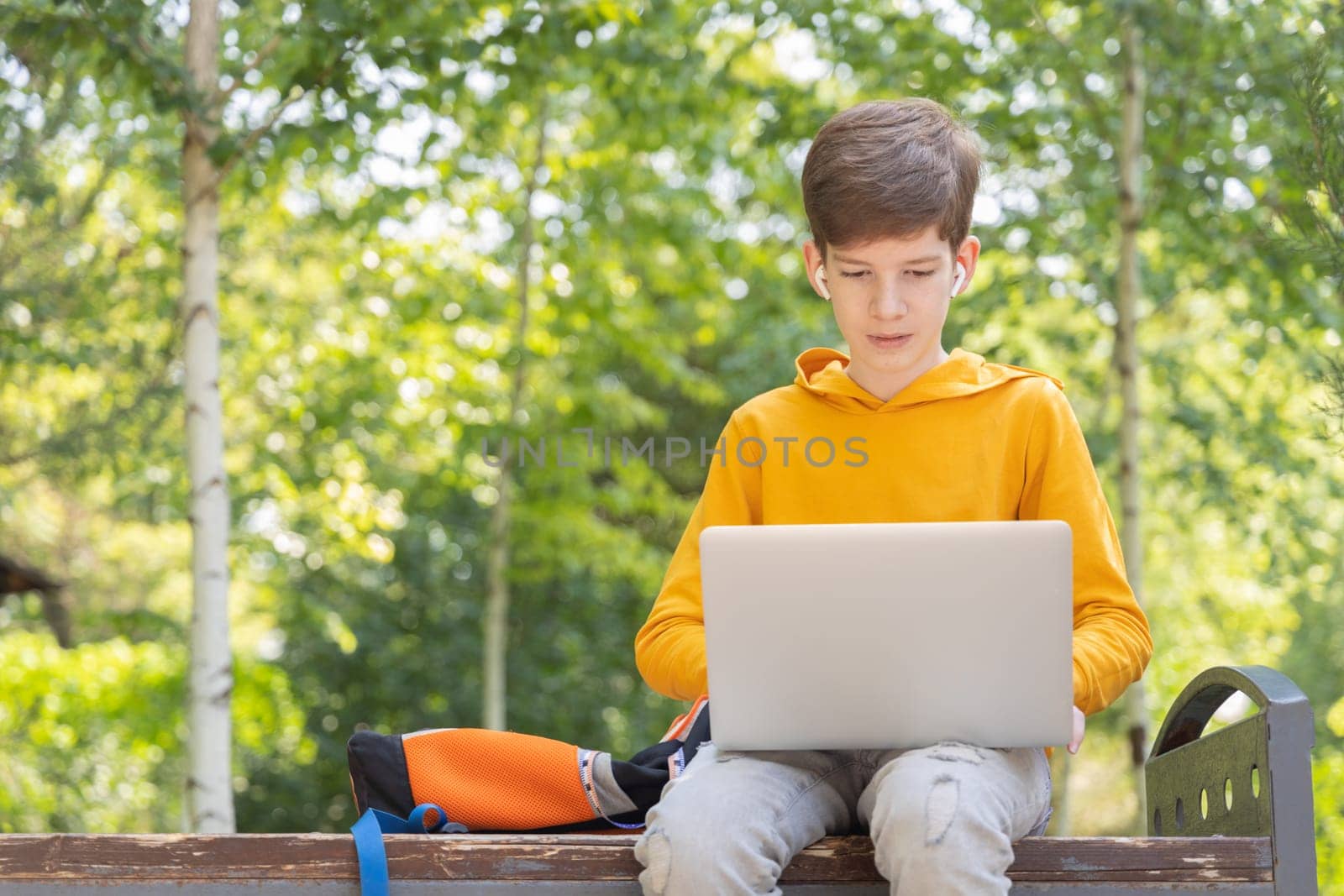 Thoughtful teenager boy working on laptop. Holding and using a laptop for networking on a sunny spring day, outdoors. by Ri6ka