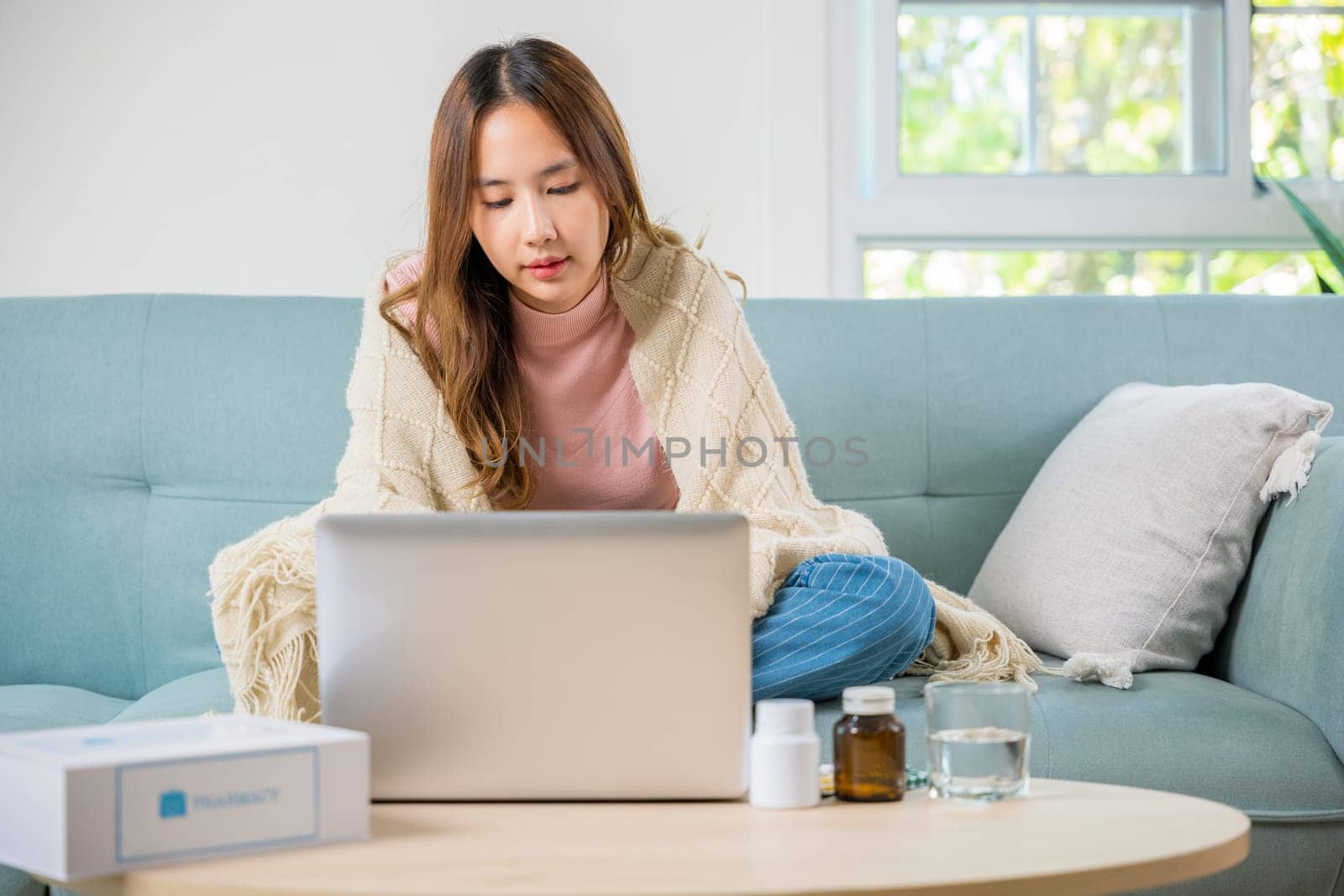 sick woman covered blanket suffering from virus but still working at home with laptop computer by Sorapop